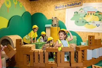 Children with yellow hard hats on and hi vis jackets playing with toy building bricks