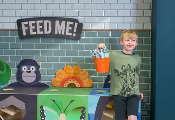 A boy holding up an orange bucket filled with toy fish to feed animals