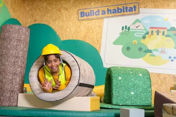 A child wearing a hard hat and hi-vis jacket crawling through a tunnel