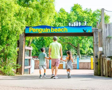 A dad and his two children walking through the Penguin beach sign
