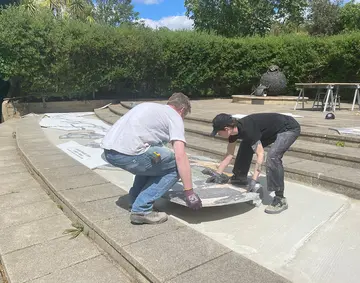 Two people installing a mosaic with greenery in the background