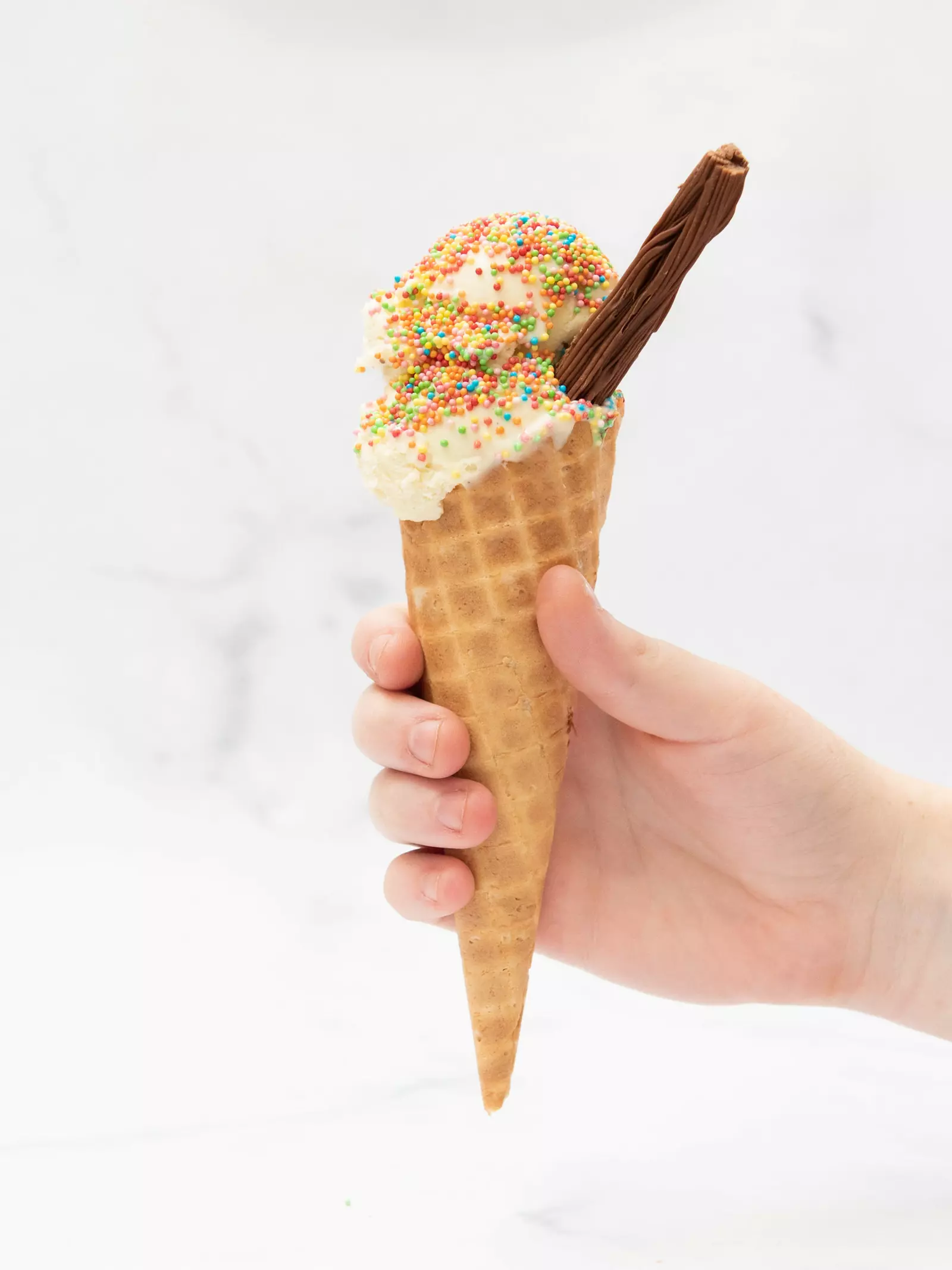 A child's hand holding an ice cream cone topped with a chocolate flake and colourful sprinkles