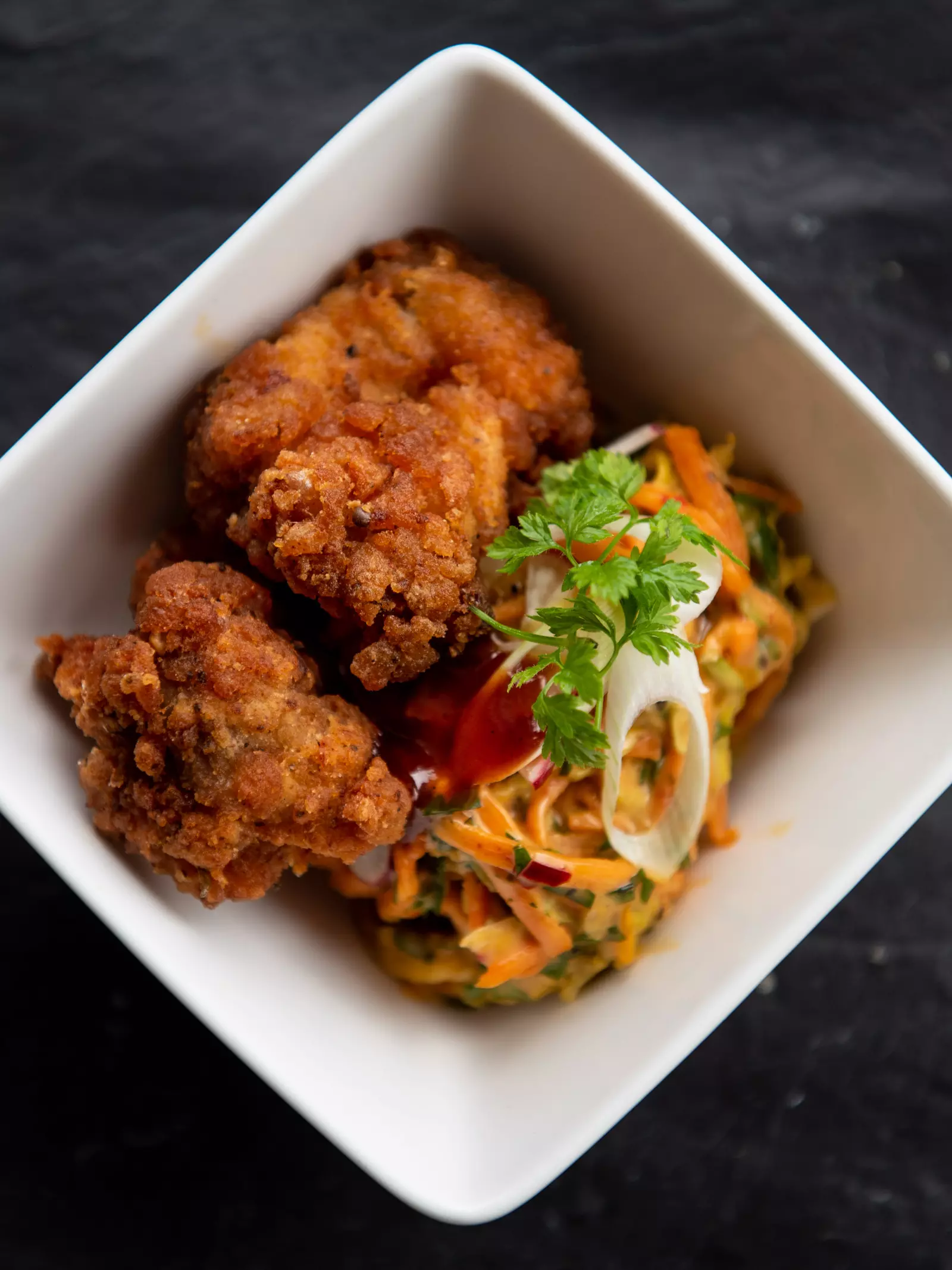 A fried chicken dish served in a bowl on a table with a fork
