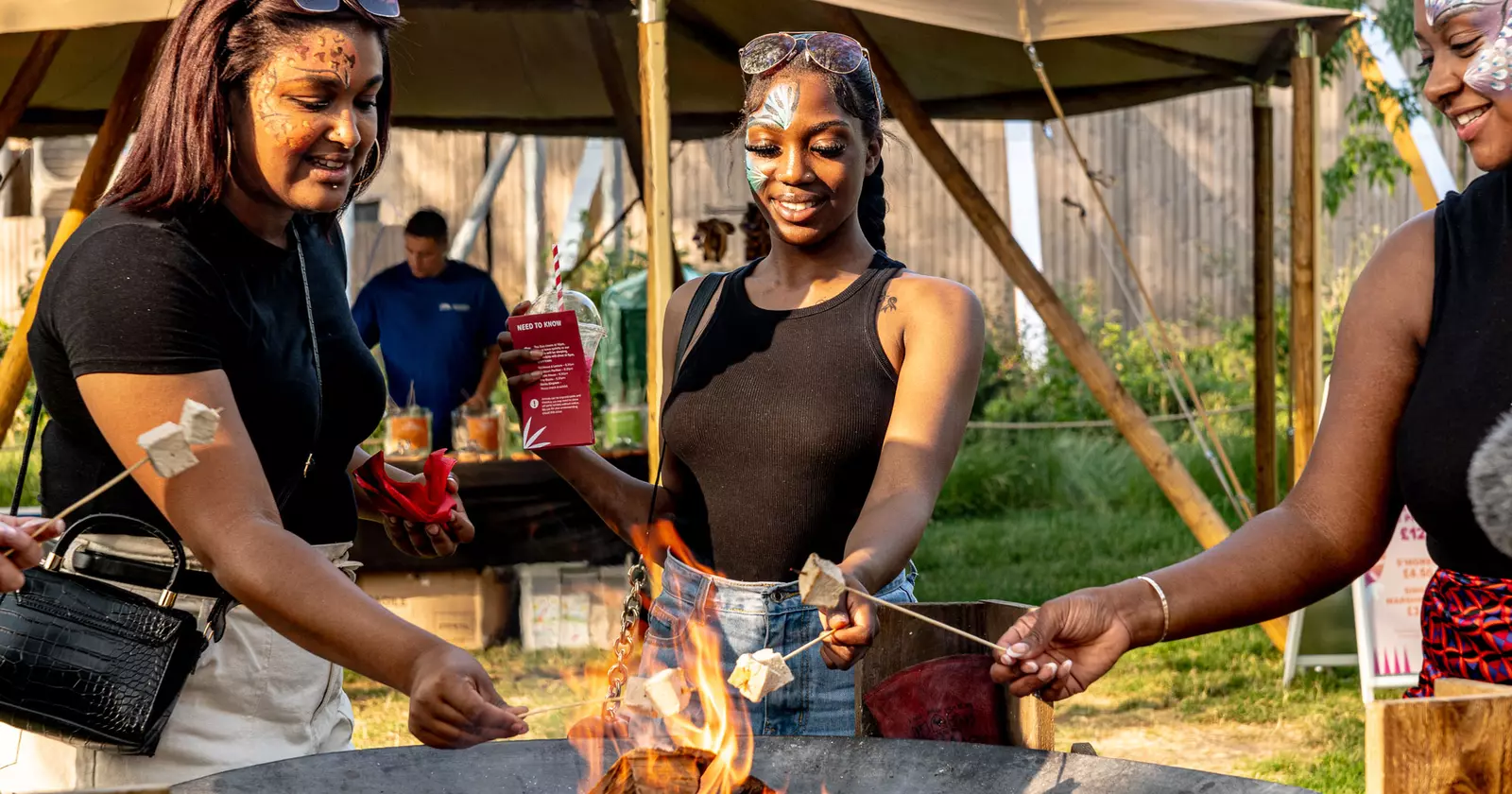 3 women roast marshmallows on sticks over an open fire