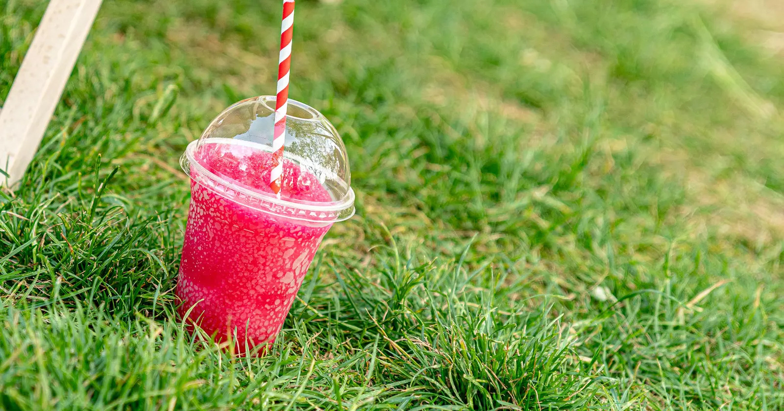 A plastic cup filled with bright red slushie mixture sits on the green grass