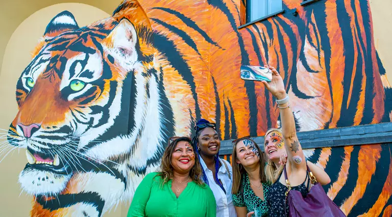 Four visitors taking a picture in front of tiger painted mural