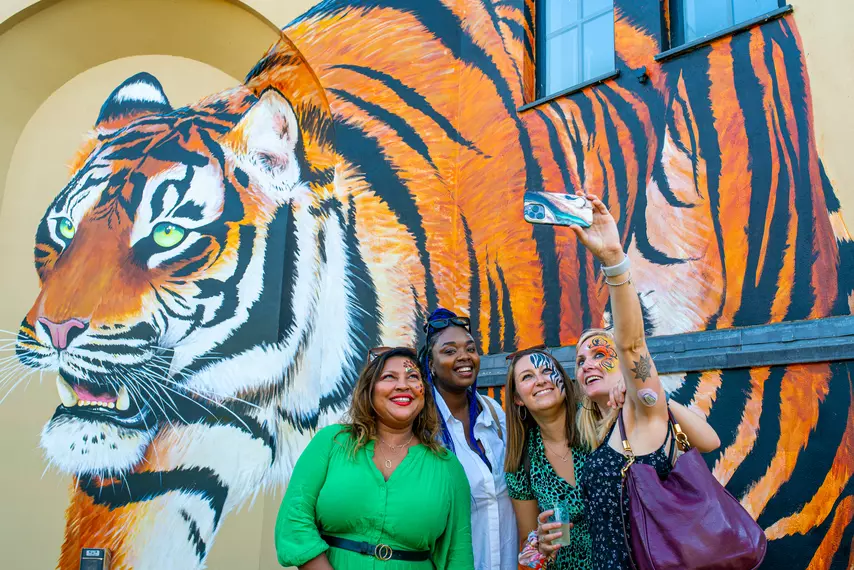 Four visitors taking a picture in front of tiger painted mural