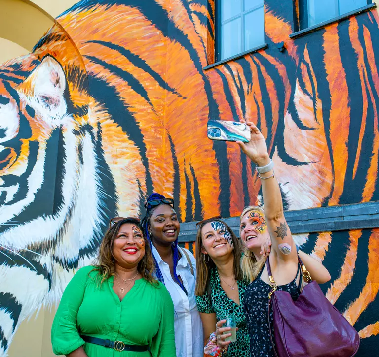 Four women posing in front of tiger mural